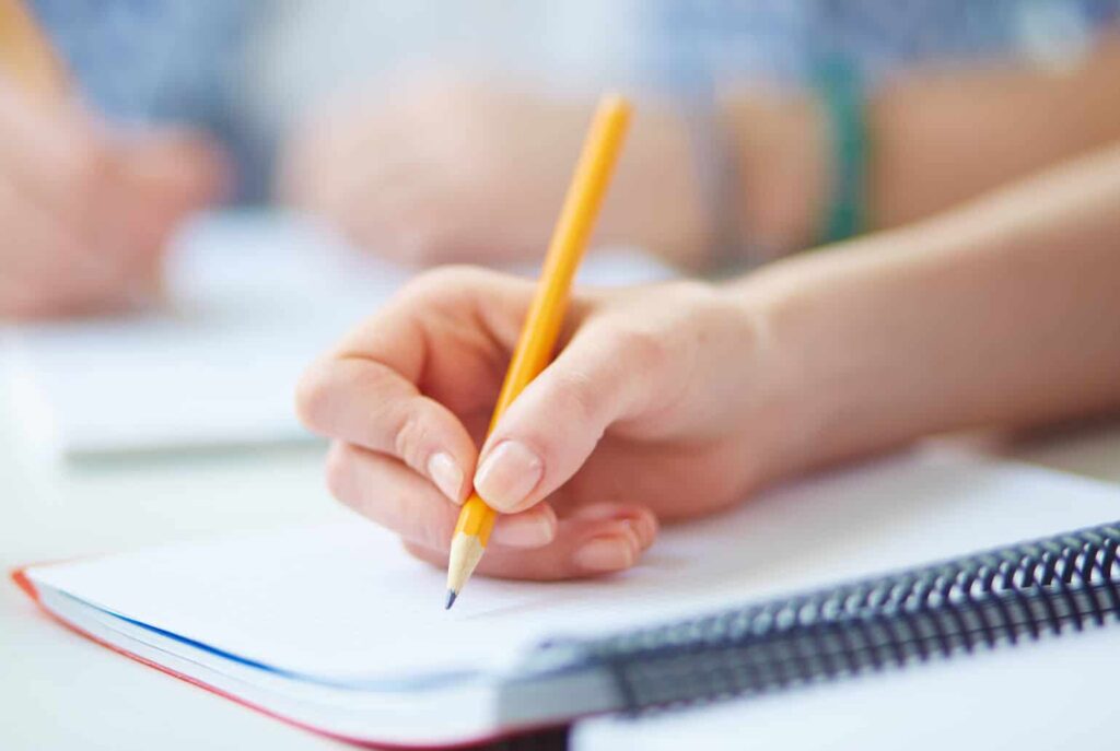 Closeup of hand with pencil, writing on notebook