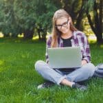 Happy young female student using laptop in park