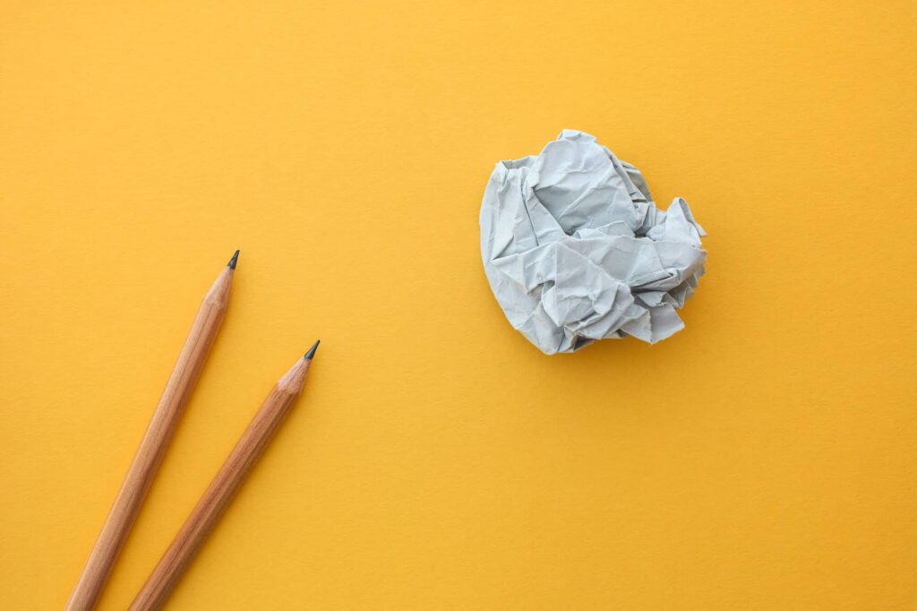 Two pencils and crumpled paper ball against yellow background