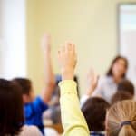 group-of-school-kids-raising-hands-in-classroom