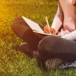 student-sitting-on-grass-writing